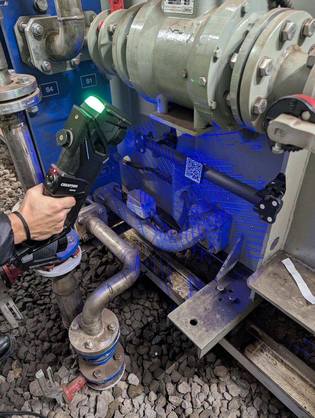 PROMECAD technician scanning industrial machinery with the Creaform HandyScan Max, projecting blue laser onto pipes and equipment